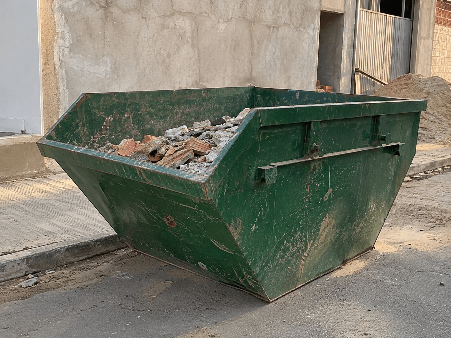 Foto ilustrativa de uma caçamba verde com entulho junto à obra